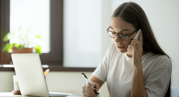 Woman on the phone whilst working at her desk.